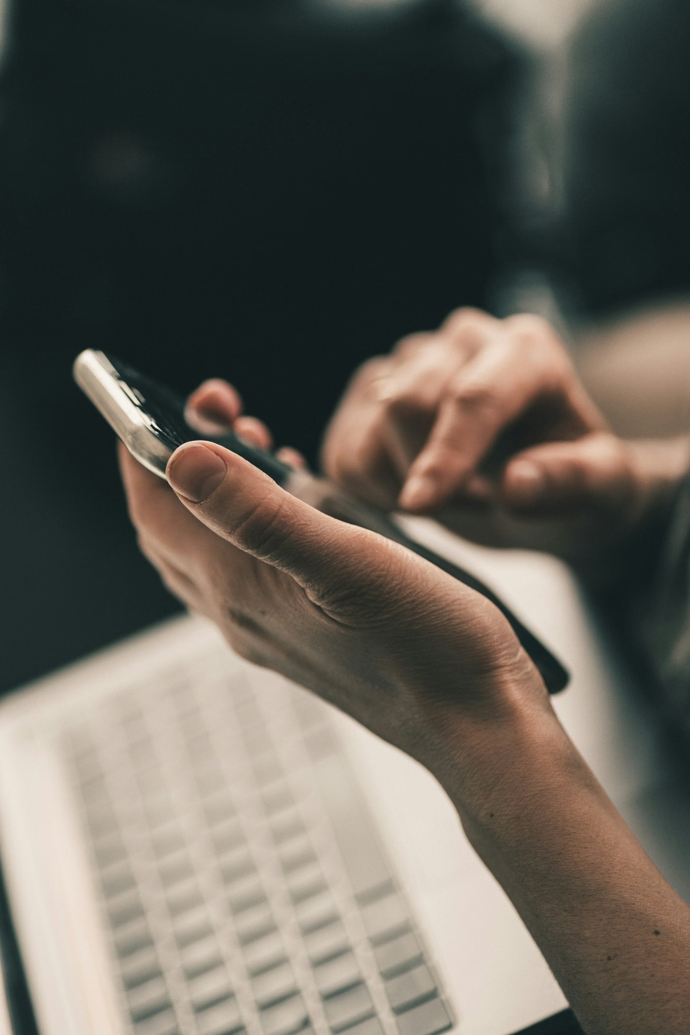 Person using a phone beside a laptop