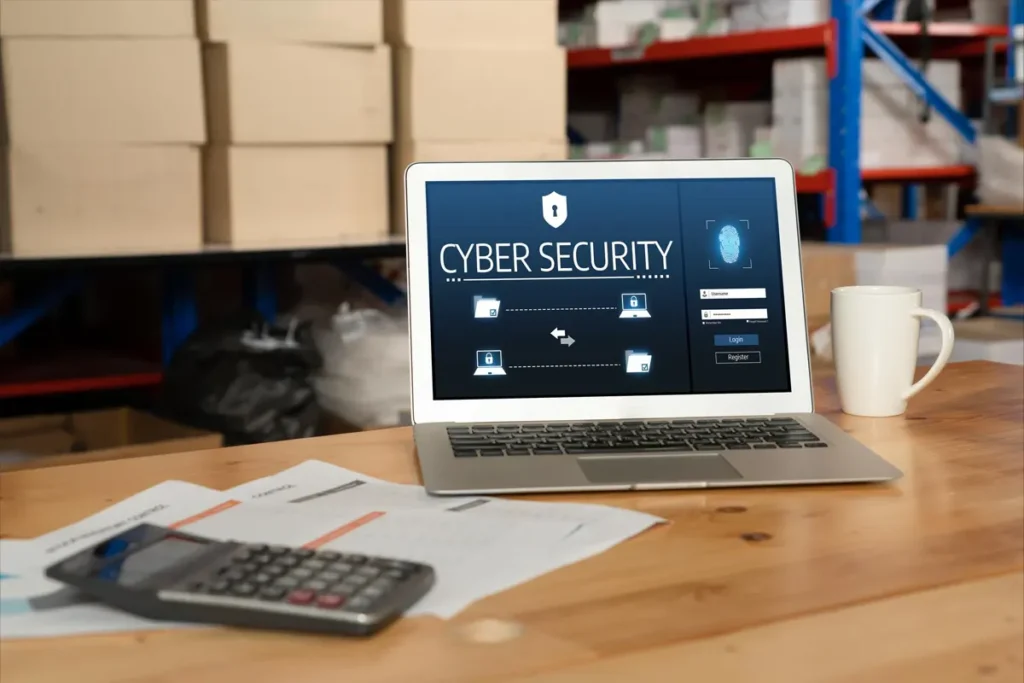 Laptop displaying a cybersecurity dashboard on a desk in a warehouse office, representing small business digital security