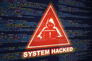 Warning graphic showing a hacker alert and “System Hacked” message over computer code, representing cyberattacks and security breaches